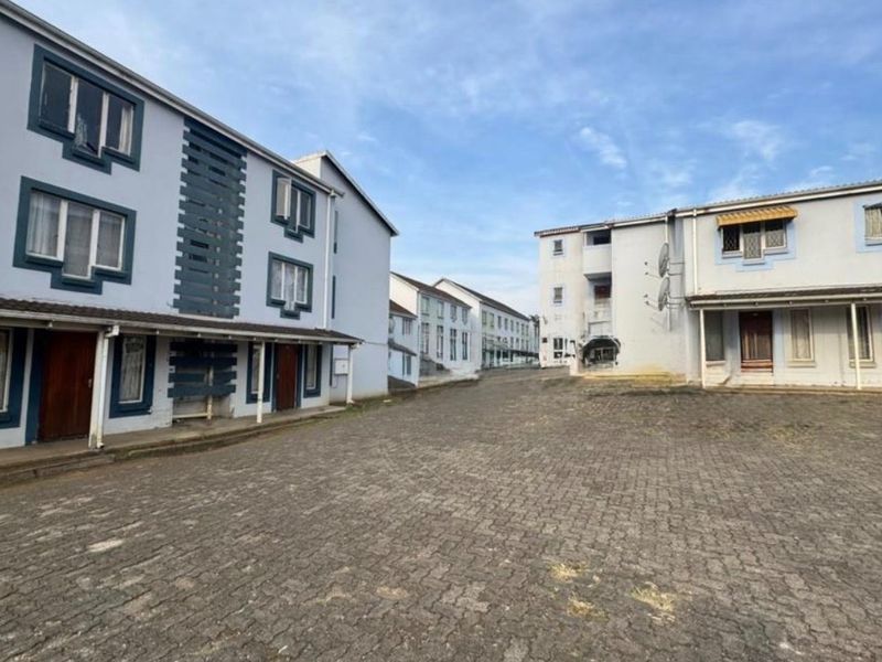 Exterior view of a multi-story apartment complex featuring cobblestone paving and covered walkways between the residential blocks.