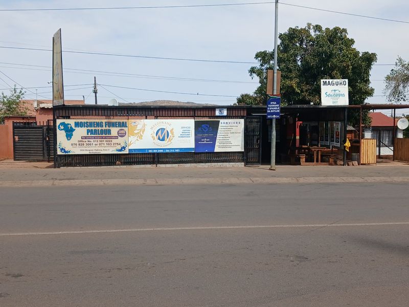Street-facing commercial property frontage featuring multiple business signs, metal security gates, and a paved entrance area.