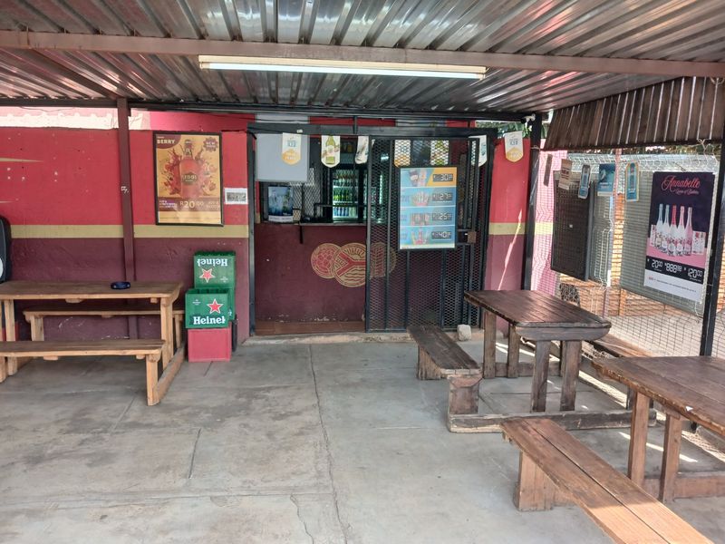 Covered outdoor patio area featuring a corrugated metal roof, concrete flooring, and a secure entrance gate, suitable for an entertainment or social space.