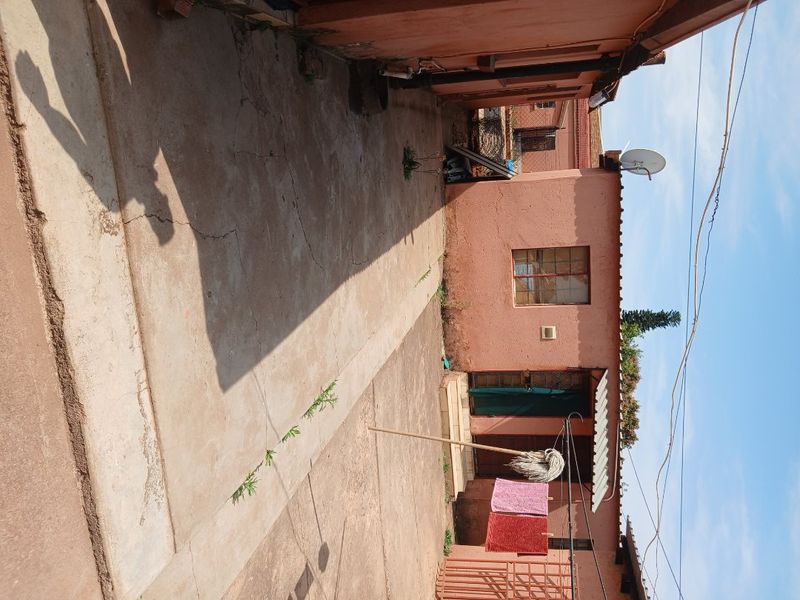 A rear exterior view of the property featuring a concrete paved courtyard area and a simple building facade with a metal window and security gate.