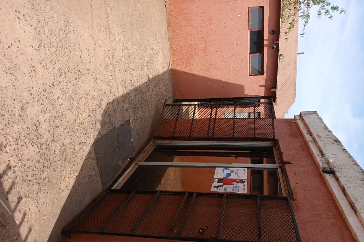 Rear exterior area featuring a concrete patio, security gate, and sliding door access with weathered wall finishes.