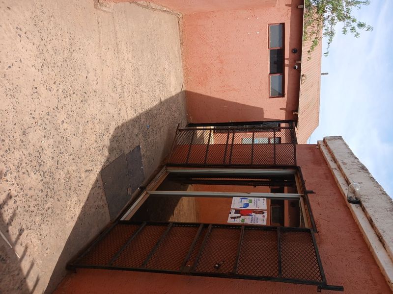Rear exterior area featuring a concrete patio, security gate, and sliding door access with weathered wall finishes.