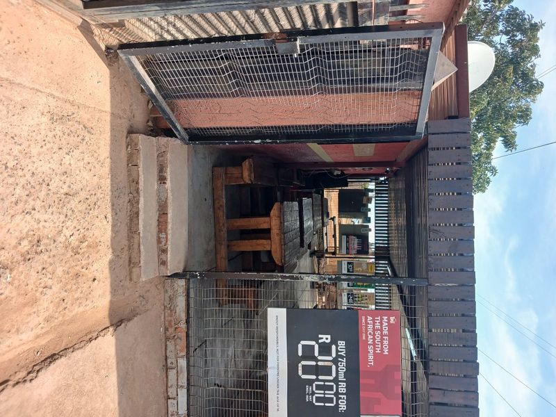 A covered outdoor patio area featuring a timber pergola structure and metal security gate access, showing signs of wear and weathering.