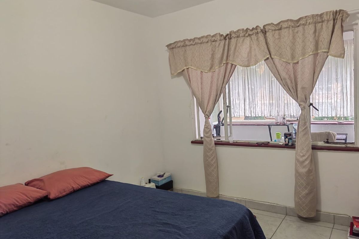 A bedroom featuring tiled flooring and a window with curtains, providing a functional space with potential for cosmetic updates.