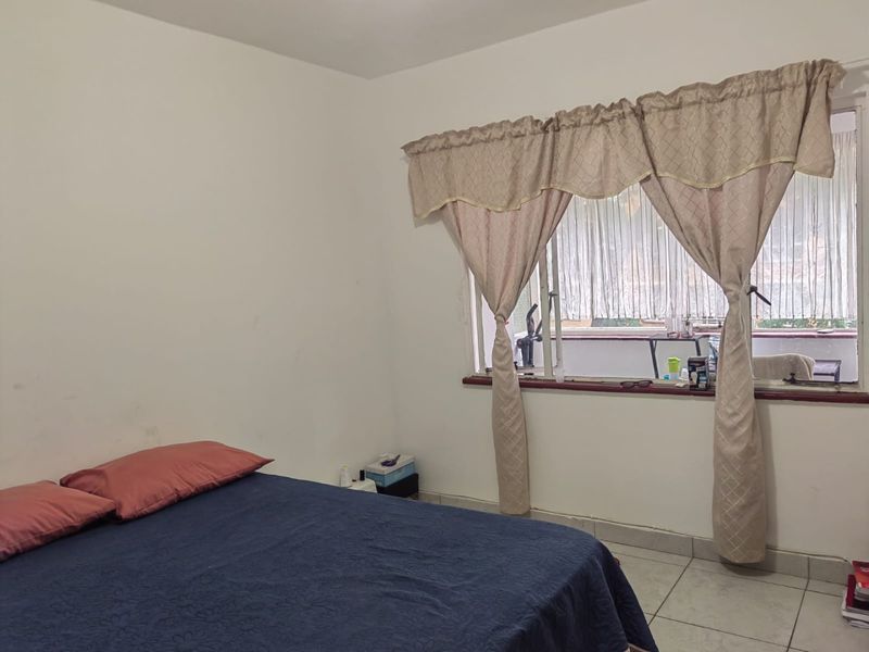 A bedroom featuring tiled flooring and a window with curtains, providing a functional space with potential for cosmetic updates.