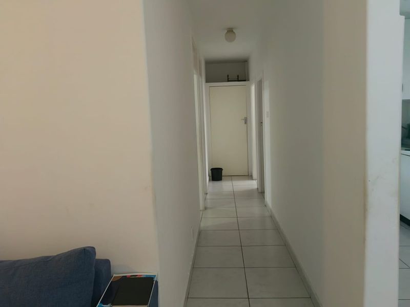 A simple, neutral hallway featuring tiled flooring and white walls, providing access to other rooms within the apartment.