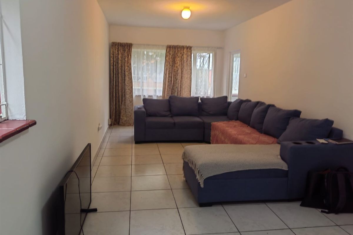 A spacious living room featuring neutral tiled flooring and large windows, providing a functional and well-lit area for relaxation.