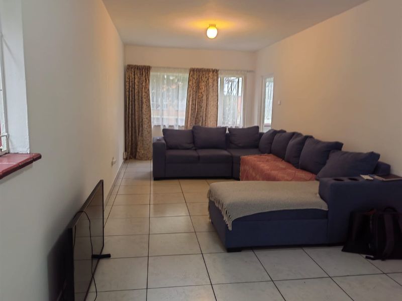 A spacious living room featuring neutral tiled flooring and large windows, providing a functional and well-lit area for relaxation.