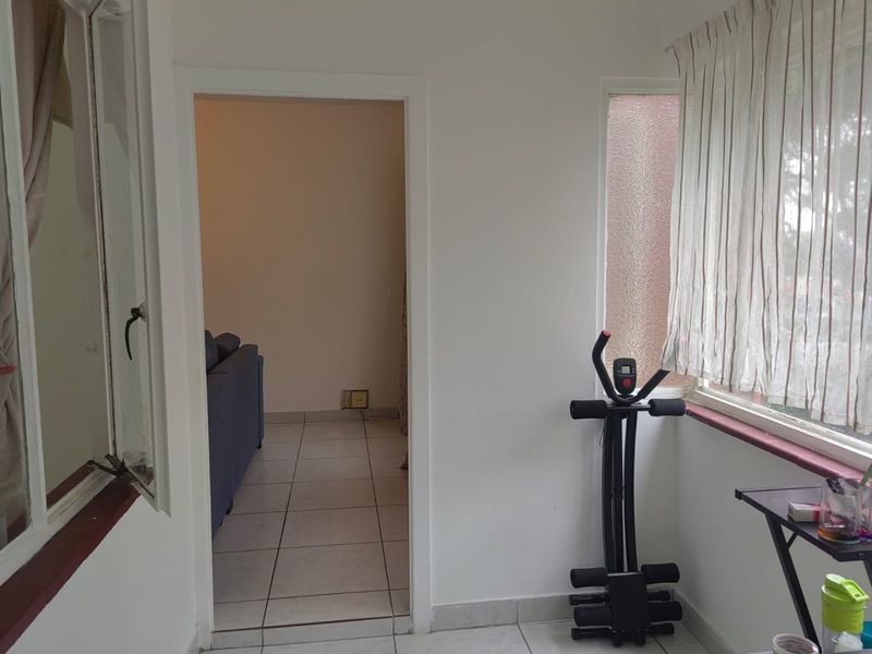 A sunroom or enclosed balcony area featuring tiled flooring and large windows, providing a transition space into the main living area of the apartment.