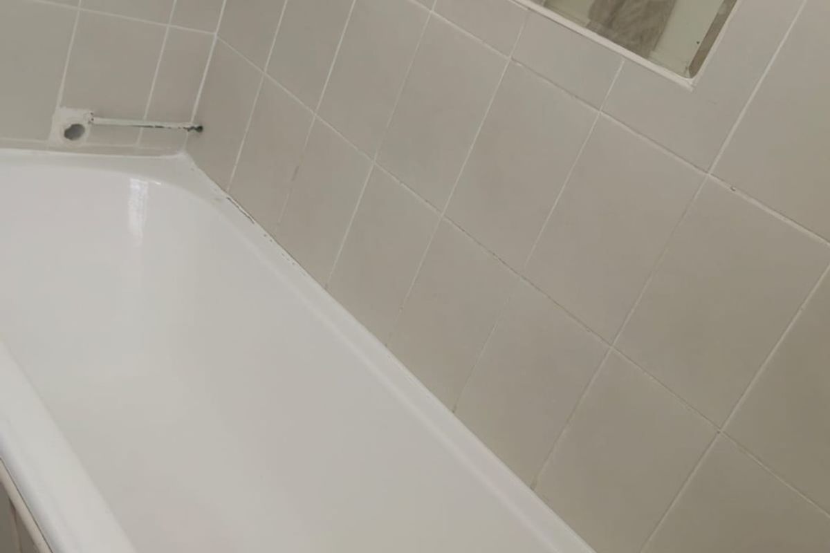 A functional bathroom featuring a standard bathtub with tiled surround, a recessed mirror, and chrome fixtures, requiring some cosmetic updates.