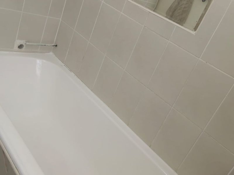 A functional bathroom featuring a standard bathtub with tiled surround, a recessed mirror, and chrome fixtures, requiring some cosmetic updates.