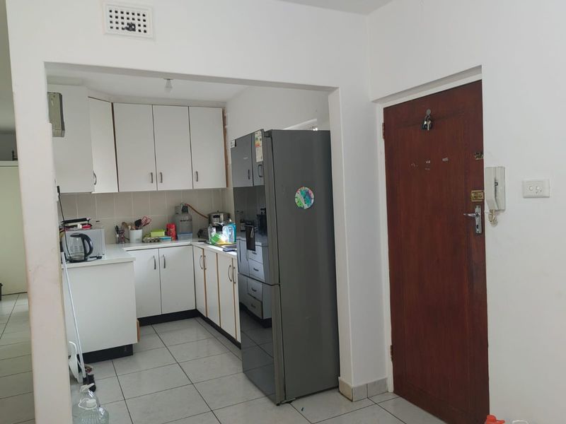 A functional kitchen featuring white built-in cabinetry, tiled flooring, and an integrated intercom system, adjacent to the main entrance door.