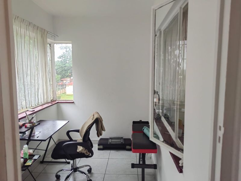 A functional office space featuring tiled flooring and large windows with security bars, offering natural light and a view of the exterior.