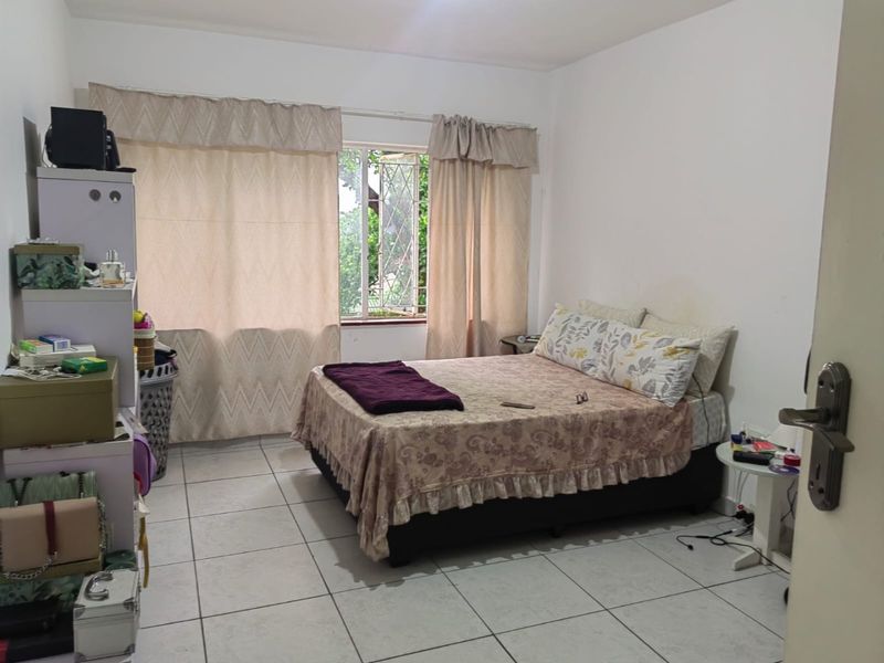 A functional bedroom featuring tiled flooring and security burglar bars on the window, providing a neutral base for potential interior updates.