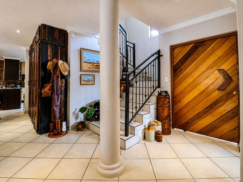 Welcoming entrance hall featuring tiled flooring, a central structural column, a wooden pivot front door, and a staircase with a decorative wrought iron balustrade.