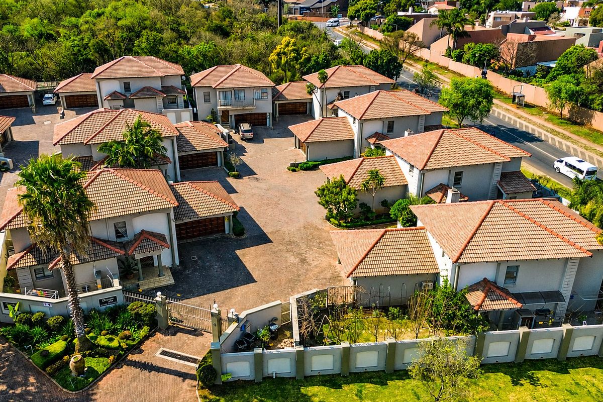 Aerial view of a residential complex featuring multiple houses with tiled roofs, paved driveways, and secure perimeter walling.