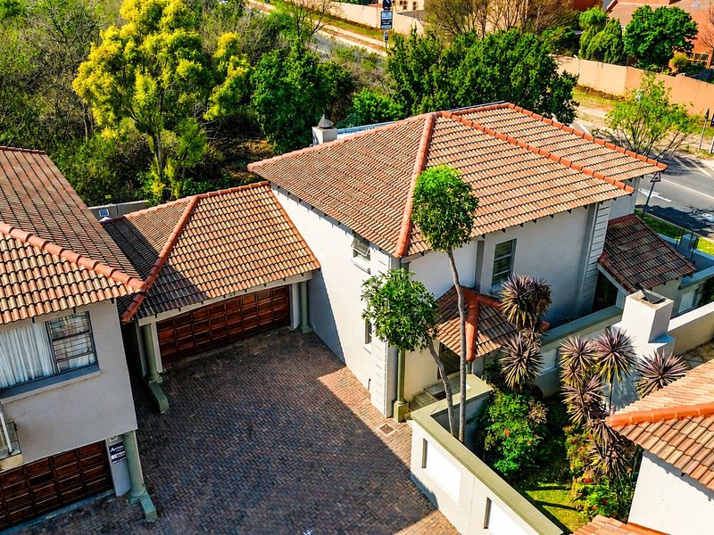 Aerial view of the property showcasing the tiled roof, paved driveway, garage access, and established garden area.