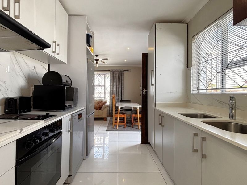 Modern galley-style kitchen featuring white cabinetry, stone countertops, integrated oven, extractor fan, and double basin sink with polished tiled flooring.