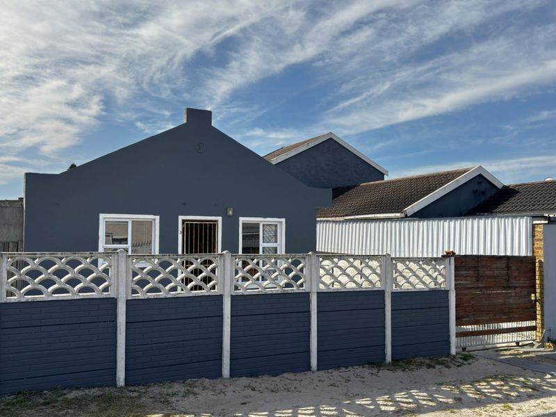 Front elevation of a residential house featuring a dark grey painted facade, tiled roof, and a precast concrete boundary wall with a secure entrance.