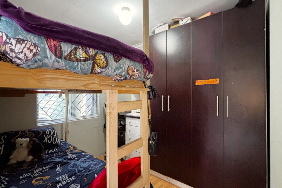 A bedroom featuring dark wood built-in cupboards and a window fitted with security bars.