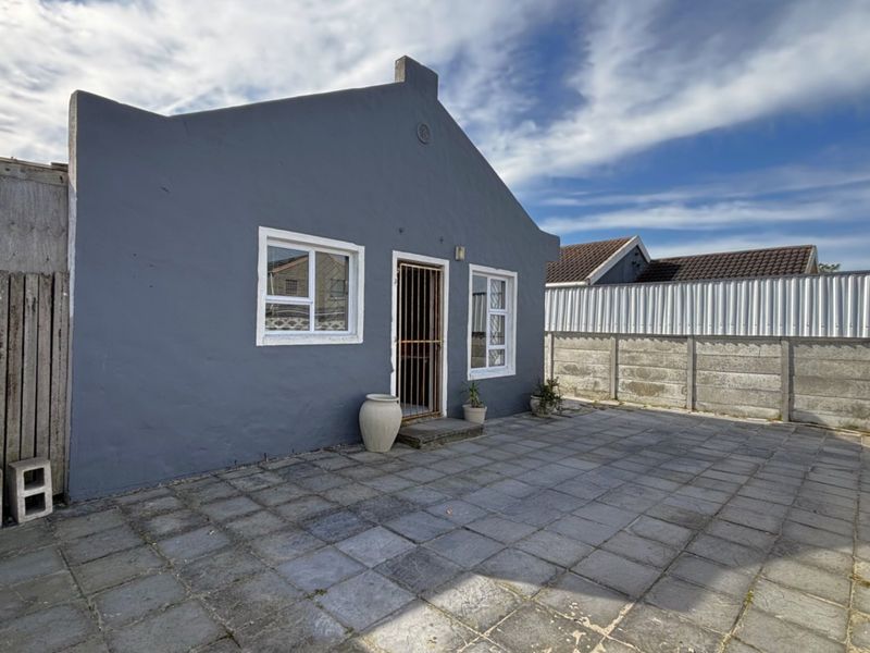 Rear exterior view of the property featuring a paved patio area, secure entrance, and perimeter boundary walls.