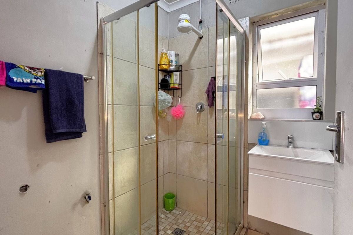 A compact bathroom featuring a shower enclosure with tiled walls and a modern wall-mounted vanity basin.