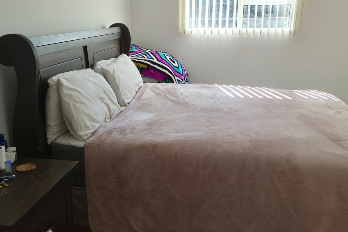 A standard bedroom featuring neutral walls and vertical window blinds, providing a functional and private sleeping space.