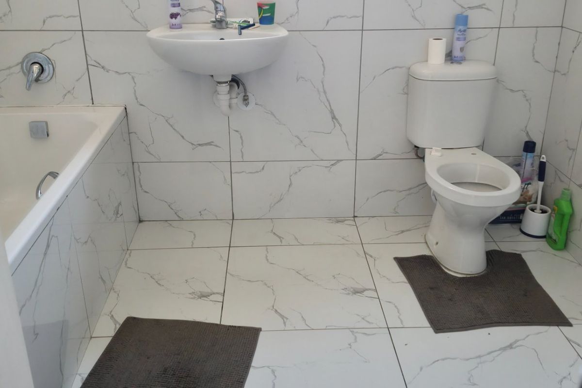 A functional bathroom featuring marble-effect tiled walls and floors, equipped with a built-in bathtub, wall-mounted basin, and standard toilet.