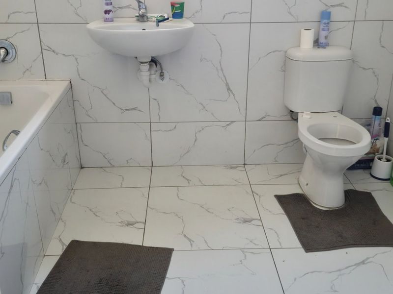 A functional bathroom featuring marble-effect tiled walls and floors, equipped with a built-in bathtub, wall-mounted basin, and standard toilet.