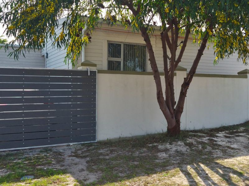 Front exterior view of the property featuring a boundary wall, sliding gate, and weatherboard cladding with an aluminium window.
