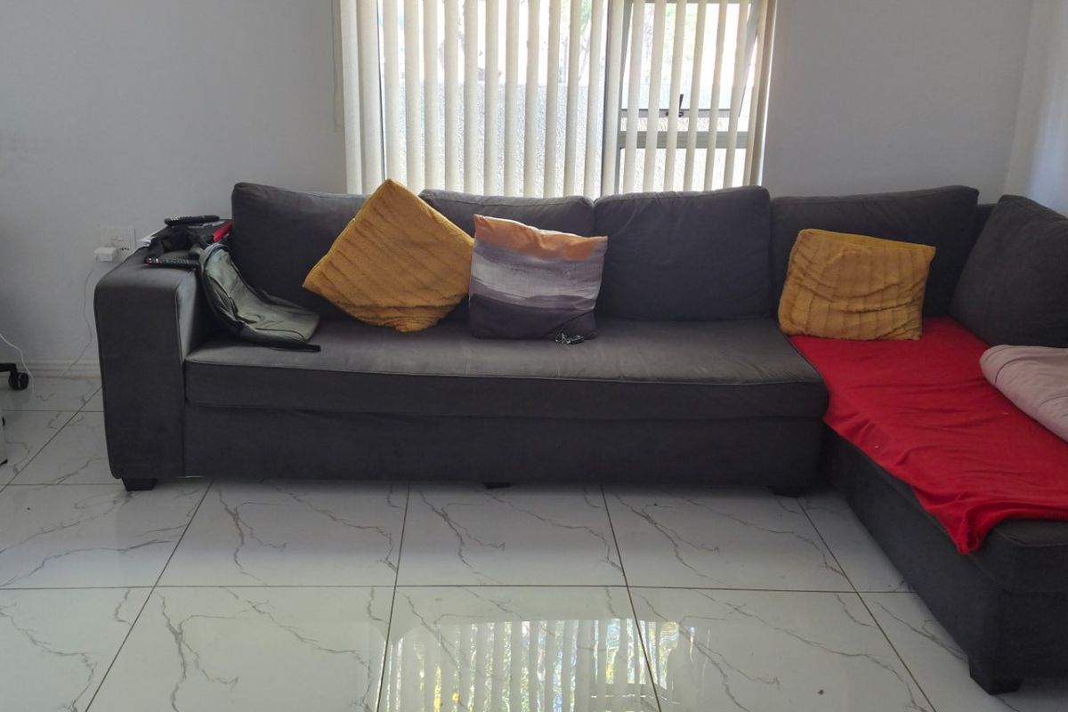 A living room featuring large marble-look floor tiles and vertical window blinds, with visible wall surface wear.