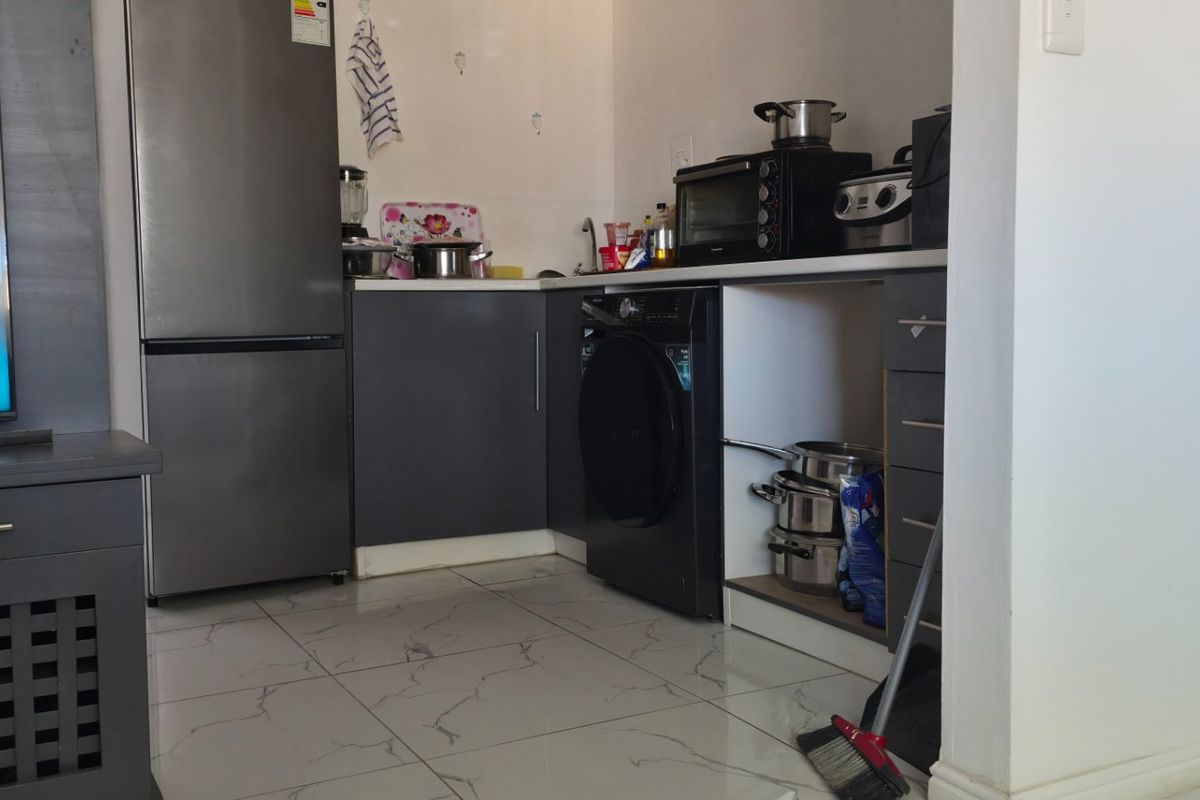 Compact kitchen area featuring dark grey cabinetry, tiled flooring, and integrated laundry appliance space, requiring minor finishing touches to the cabinetry.