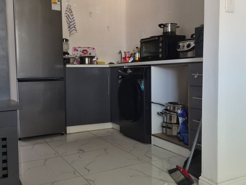 Compact kitchen area featuring dark grey cabinetry, tiled flooring, and integrated laundry appliance space, requiring minor finishing touches to the cabinetry.