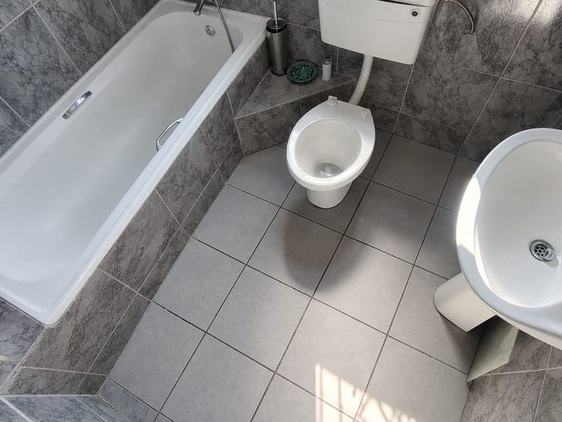 A functional bathroom featuring a bathtub, pedestal sink, and toilet with grey tiled walls and flooring.
