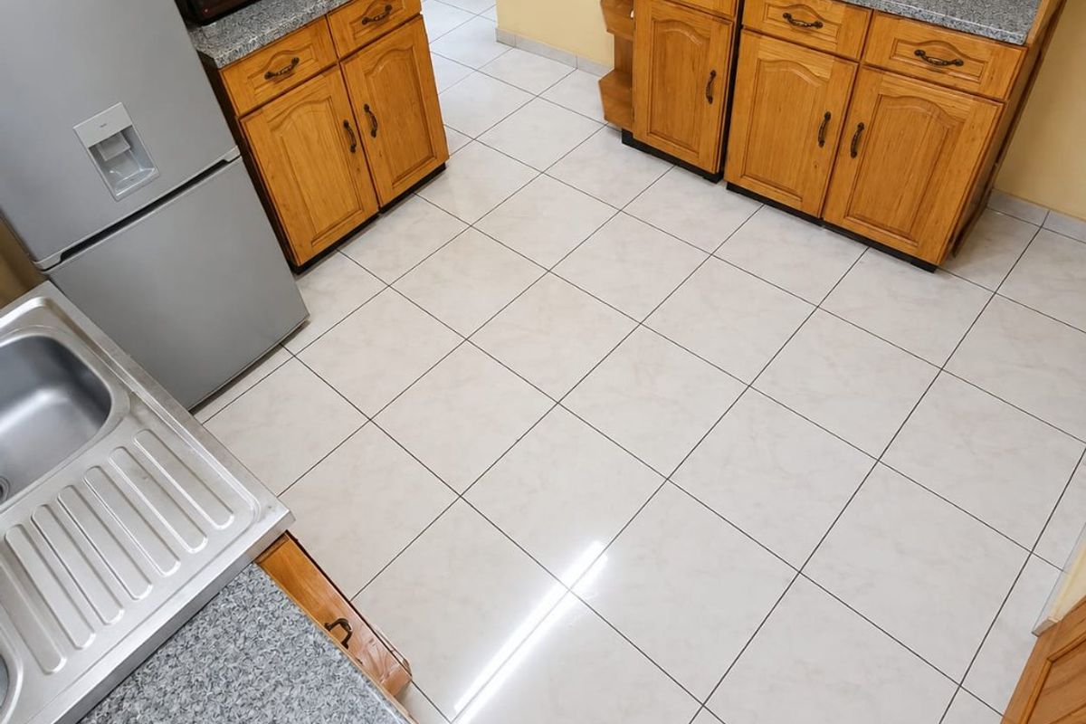 A functional kitchen featuring wooden cabinetry, granite countertops, and tiled flooring, providing a practical workspace with ample storage.