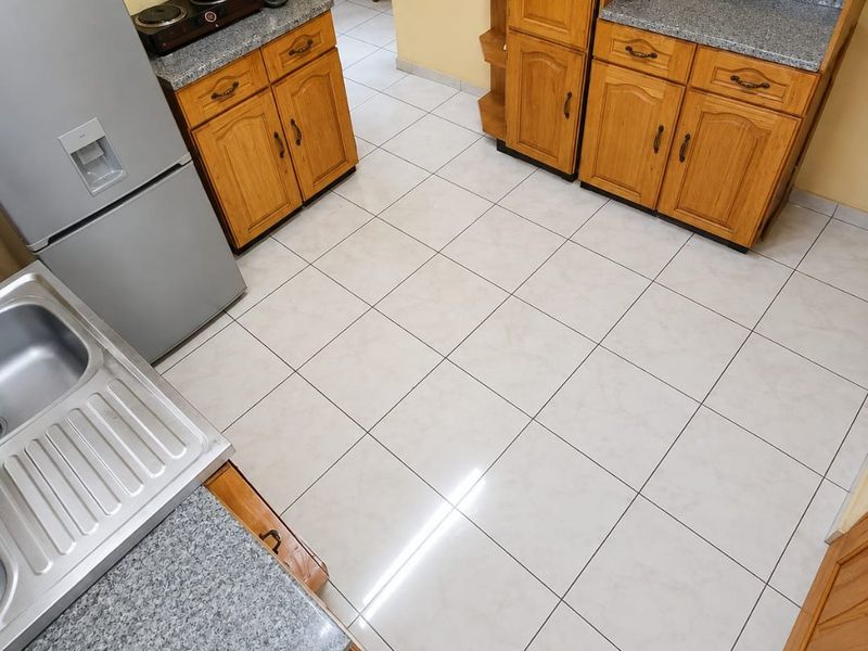 A functional kitchen featuring wooden cabinetry, granite countertops, and tiled flooring, providing a practical workspace with ample storage.