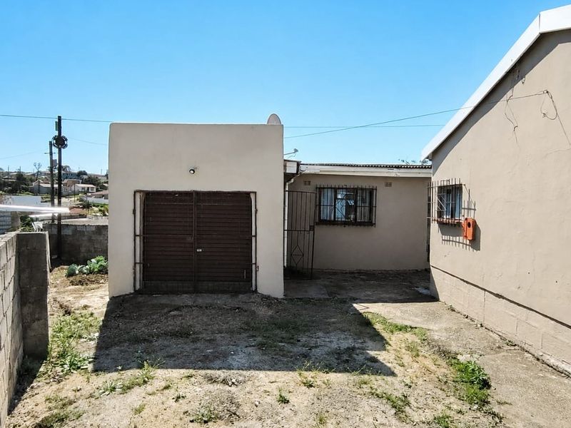 Rear exterior view of the property featuring a detached garage, concrete paving, and boundary walling in a residential setting.