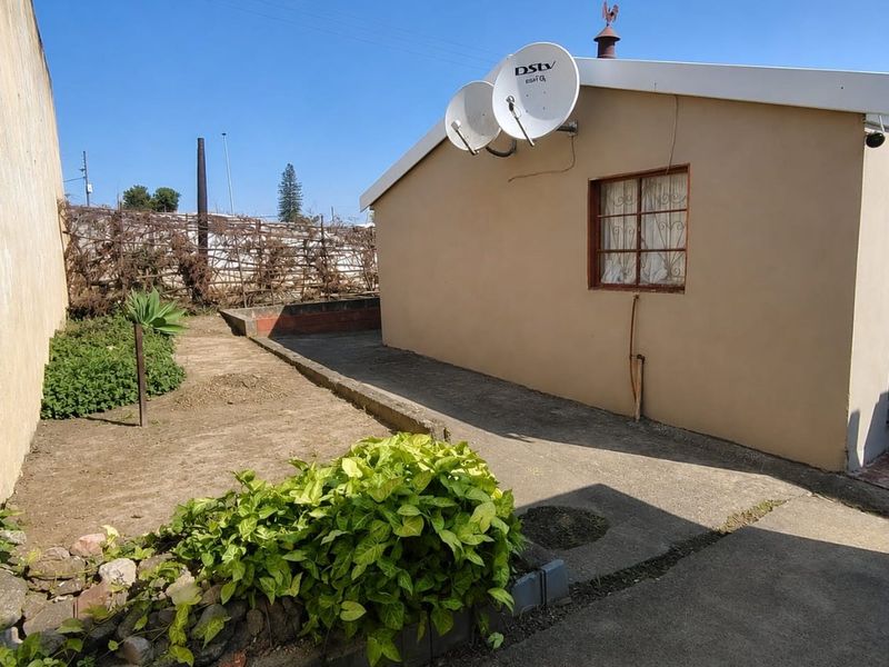 Rear exterior view of the property featuring a concrete paved area, garden bed, and satellite dish mounted on the gable wall.