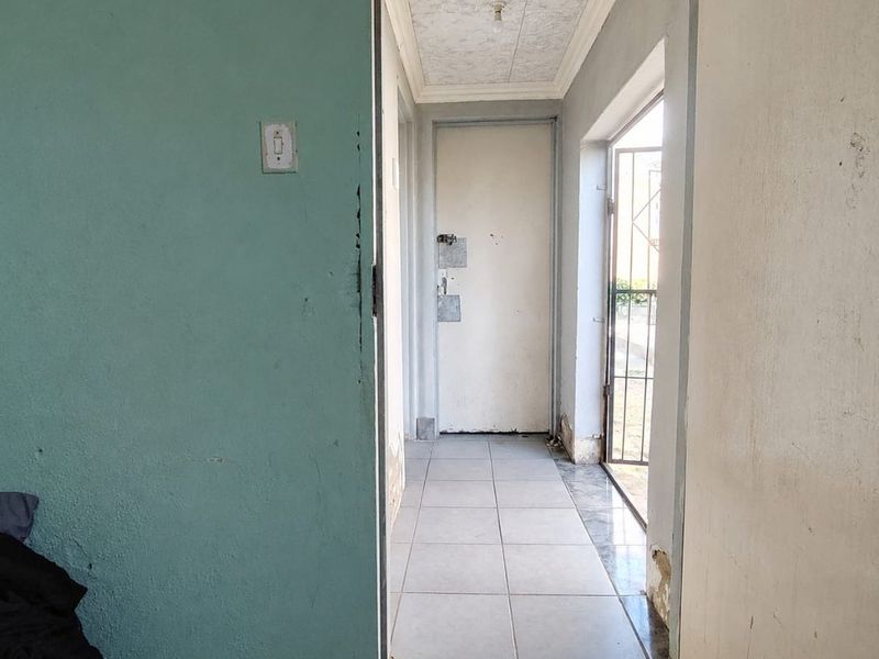 A functional hallway featuring tiled flooring, a security gate, and ceiling tiles, showing signs of wear and requiring cosmetic updates.