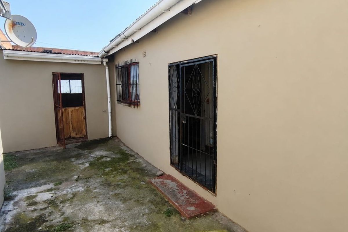 Rear exterior view of the property featuring concrete paving, security gates, and security bars on windows.