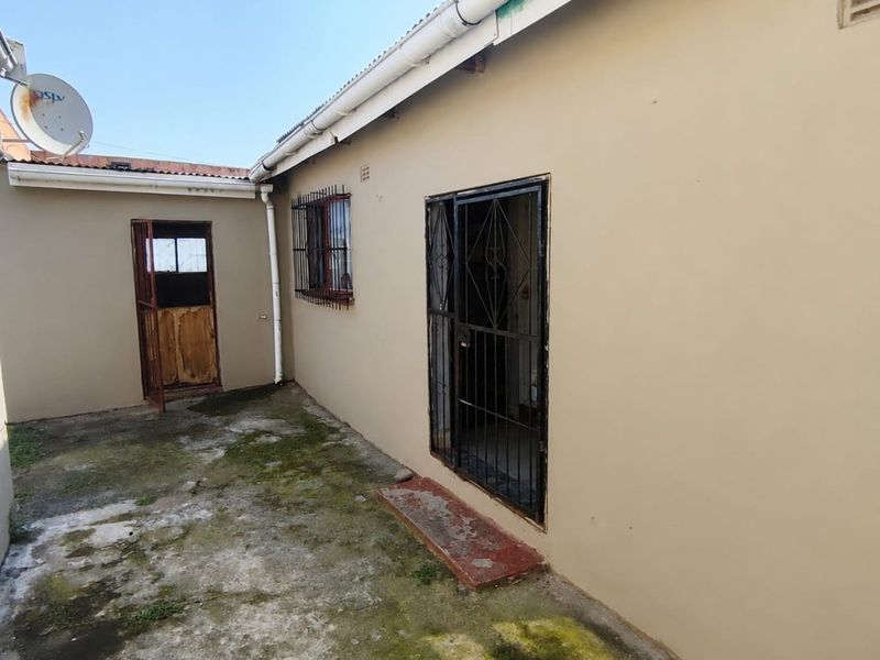 Rear exterior view of the property featuring concrete paving, security gates, and security bars on windows.
