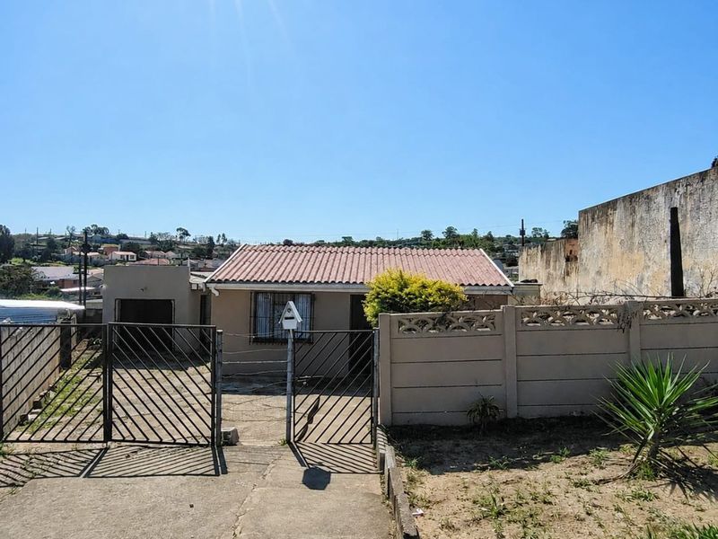 Front exterior view of a single-story house featuring a tiled roof, concrete driveway, and secure metal gate with perimeter boundary walling.