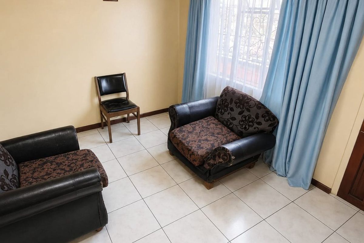 A living room featuring light-colored floor tiles, a timber-paneled ceiling, and large windows fitted with security bars.