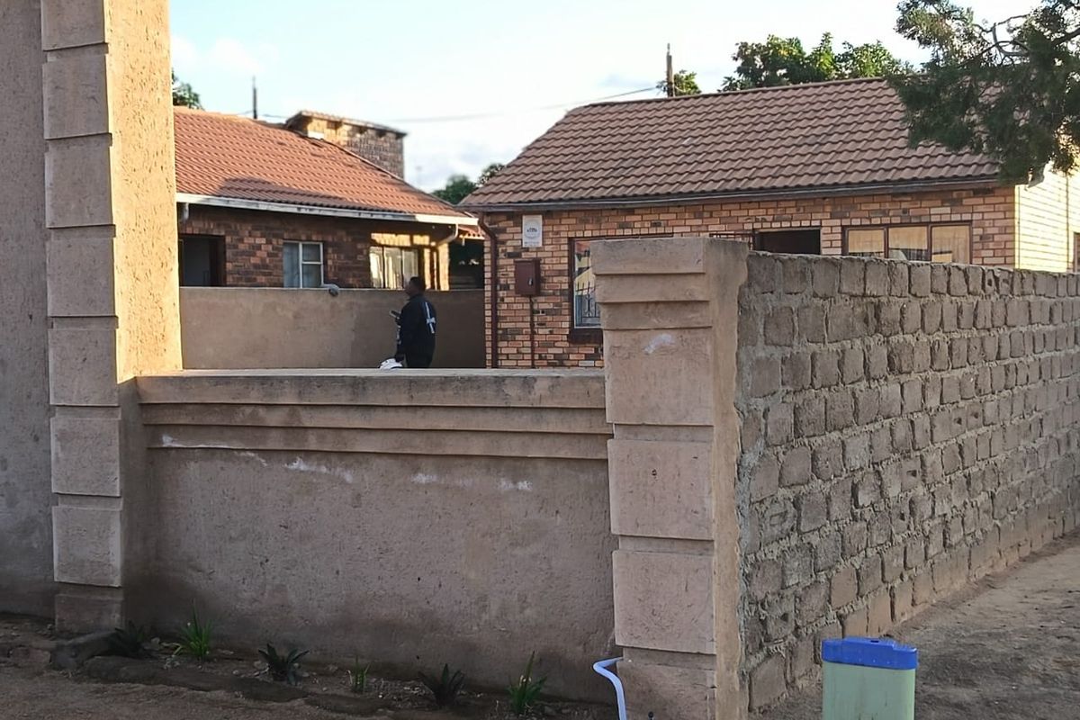 Front view of a residential property featuring a brick facade, tiled roof, and a partially finished perimeter boundary wall.