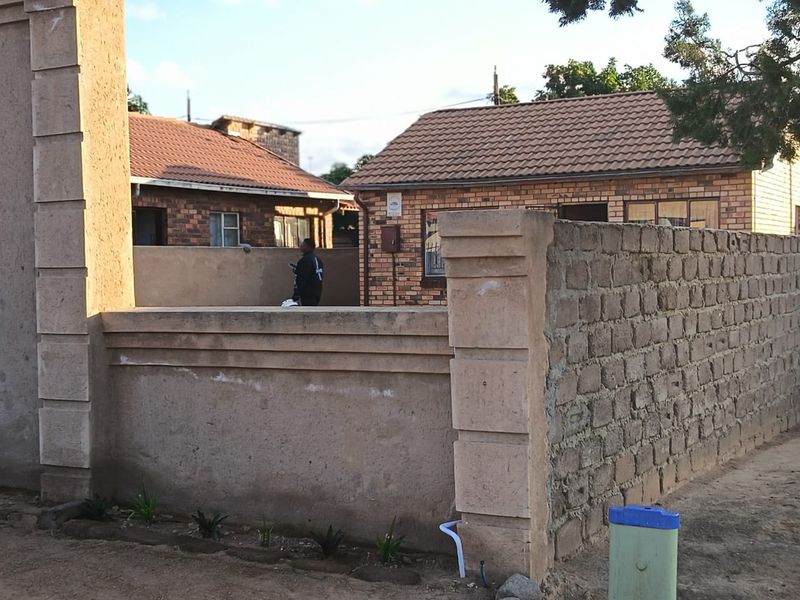 Front view of a residential property featuring a brick facade, tiled roof, and a partially finished perimeter boundary wall.