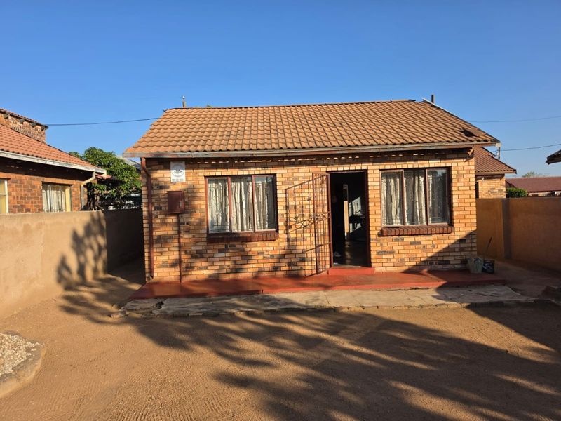 Front elevation of a face brick house featuring a tiled roof, security gate, and a concrete patio area.