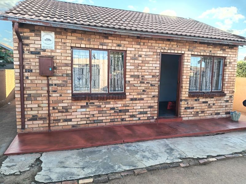 Front elevation of a face brick house featuring a tiled roof, security bars on windows, and a concrete apron entrance.