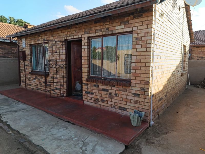 Front exterior view of a face brick house featuring a tiled roof, security gate, and a concrete porch area.