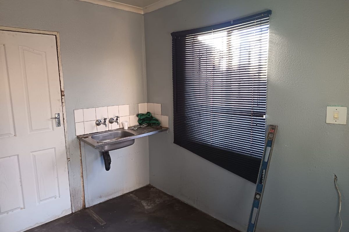 A basic utility or laundry area featuring a stainless steel sink, tiled splashback, and venetian blinds, currently in need of cosmetic refurbishment.
