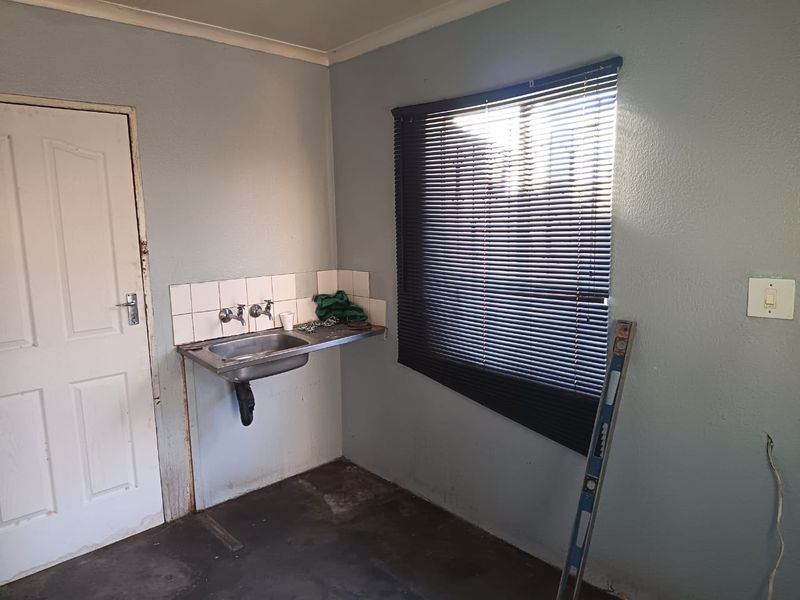 A basic utility or laundry area featuring a stainless steel sink, tiled splashback, and venetian blinds, currently in need of cosmetic refurbishment.